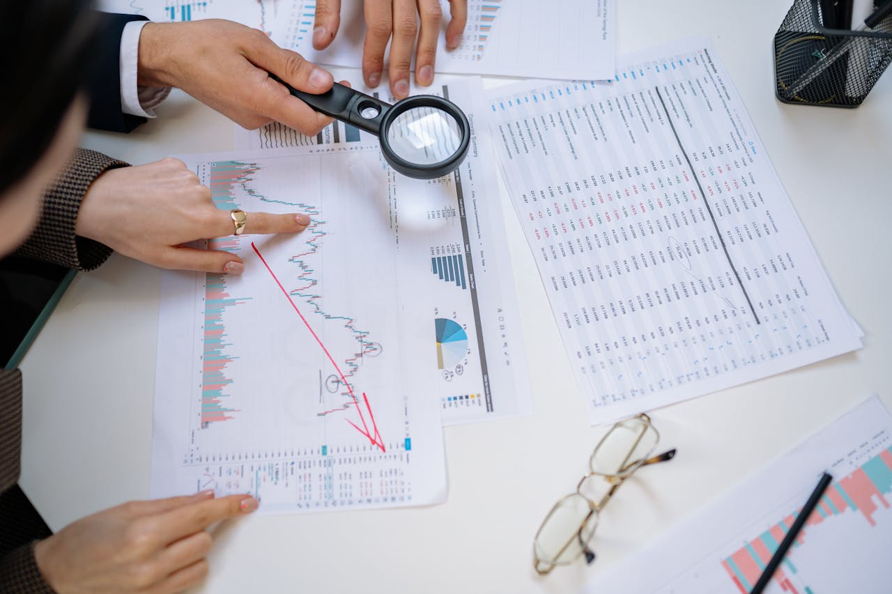 hero-img-02 Business professionals examining financial documents with magnifying glass for detailed analysis.